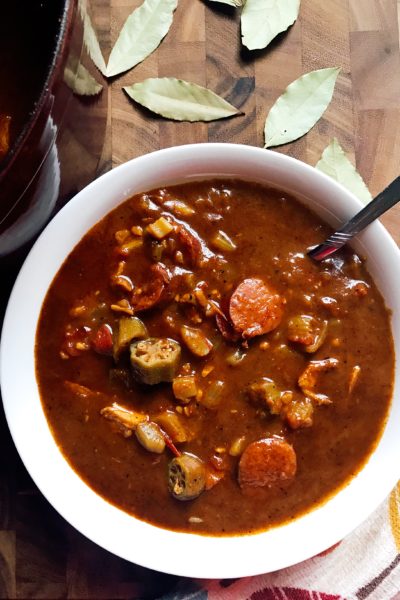A bowl of Authentic Chicken and Smoked Sausage Gumbo with bay leaves around it