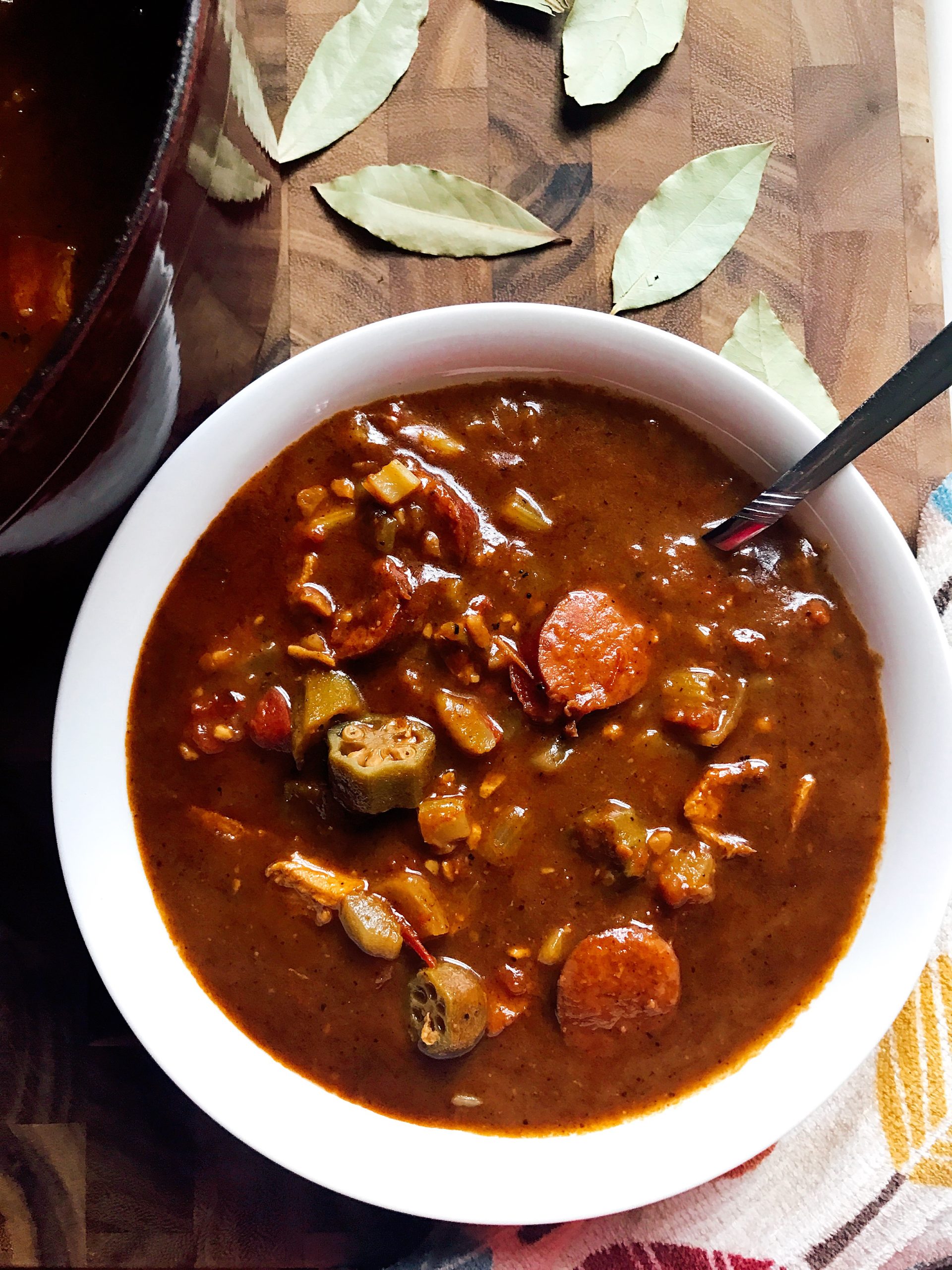 A bowl of Authentic Chicken and Smoked Sausage Gumbo with bay leaves around it