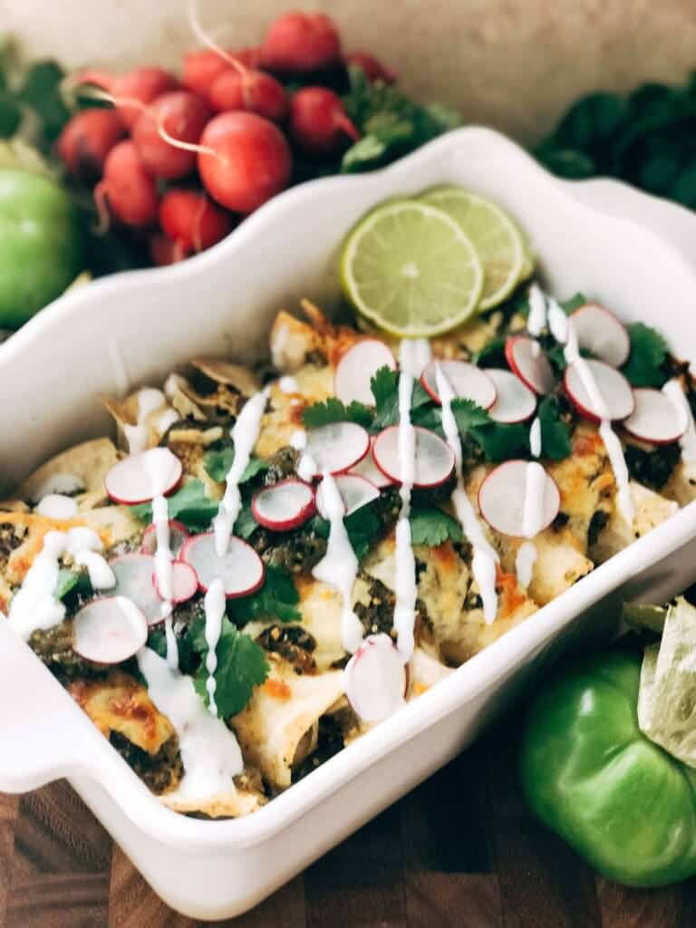 A white dish filled with Roasted Poblano Salsa Verde Green Enchiladas with Chicken with vegetables around it
