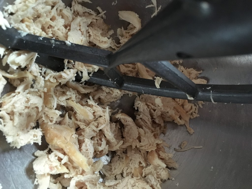 Chicken being shredded in the bowl of a stand mixer