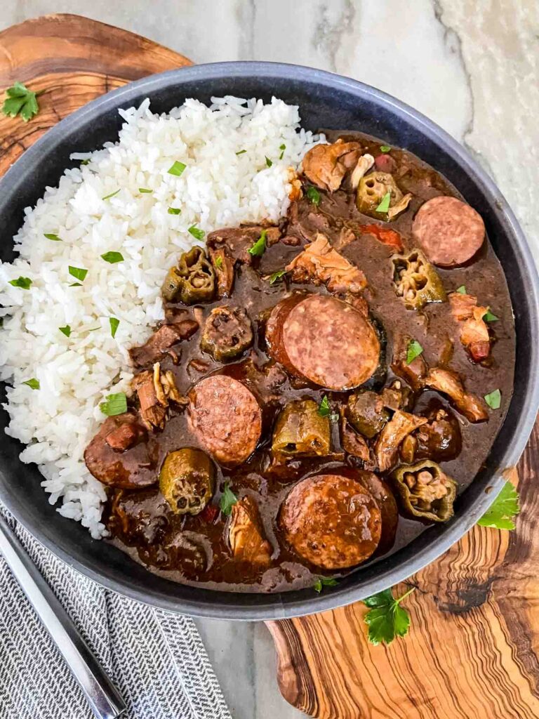 Straight from NOLA, this Authentic Chicken and Smoked Sausage Gumbo is a cold weather staple in our house. Smoky flavors will make this a favorite when you are craving soup or stew. Whether you make it spicy or mild, it is great for game day! | Three Olives Branch | www.threeolivesbranch.com Top view of Authentic Chicken and Smoked Sausage Gumbo in a gray bowl with rice