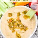 Pin of Roasted Hatch Green Chile Hummus in a small bowl with some peppers garnished on top. A hand dunking a piece of celery into the hummus. Title is listed at the top.