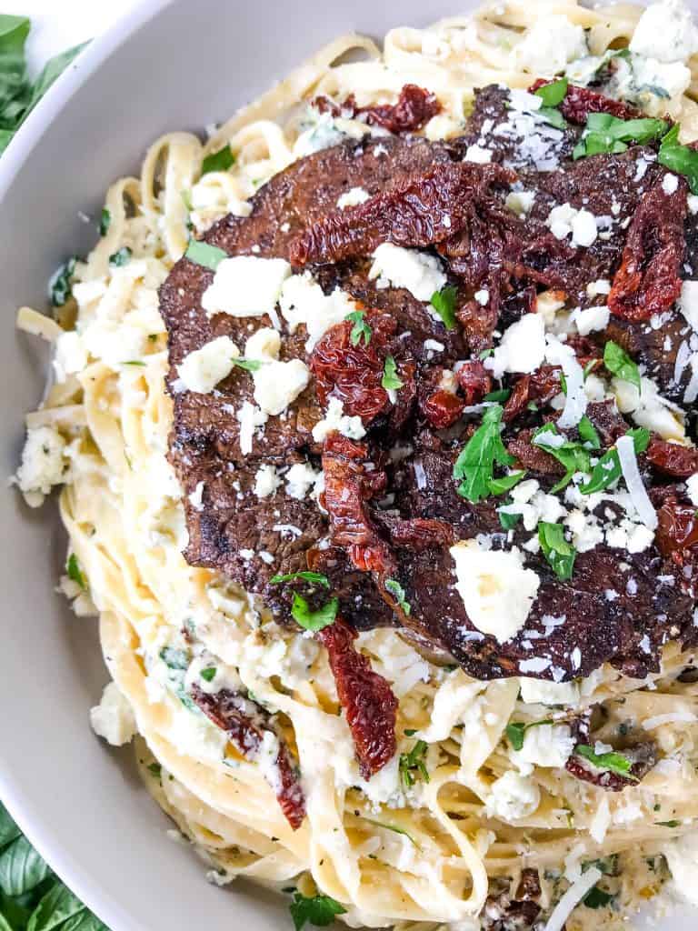 Close up of steak, tomatoes, and cheese piled up on top of creamy pasta