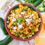 Mexican Street Corn Salsa (Esquites) in a bowl on a counter from the top view with peppers and chips around it