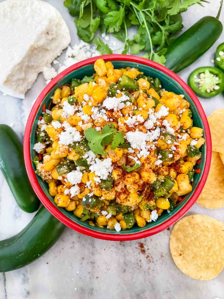 Mexican Street Corn Salsa (Esquites) in a bowl on a counter from the top view with peppers and chips around it