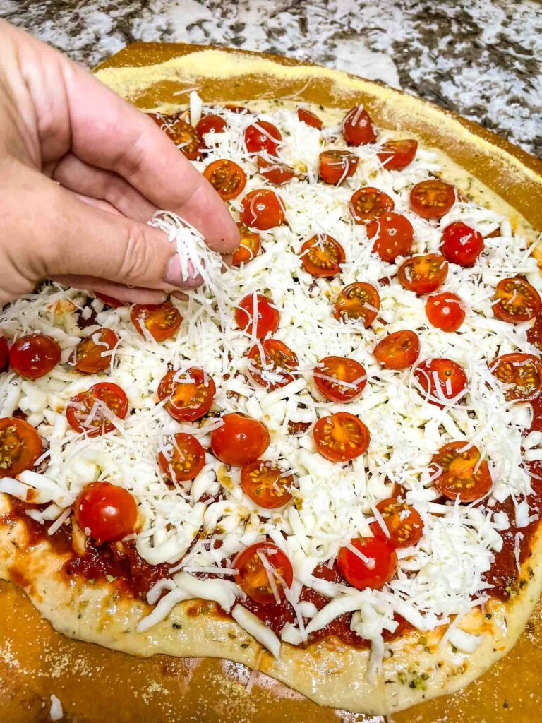 A hand sprinkling cheese onto the pizza