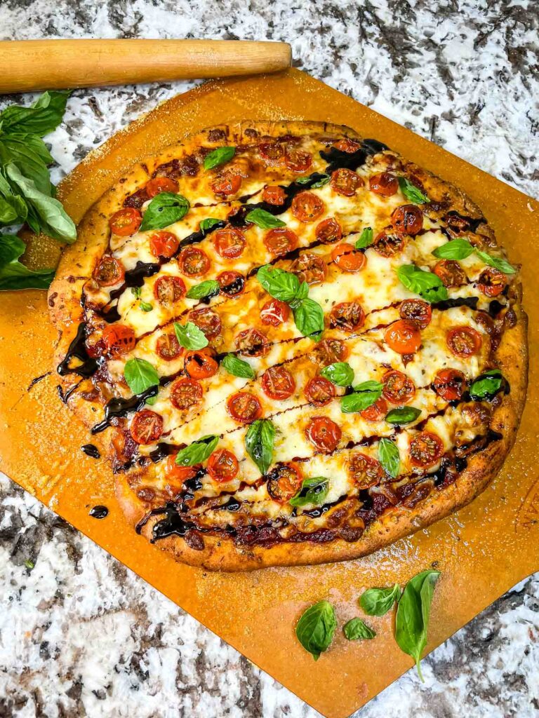 Caprese Pizza on a peel with drizzle balsamic vinegar