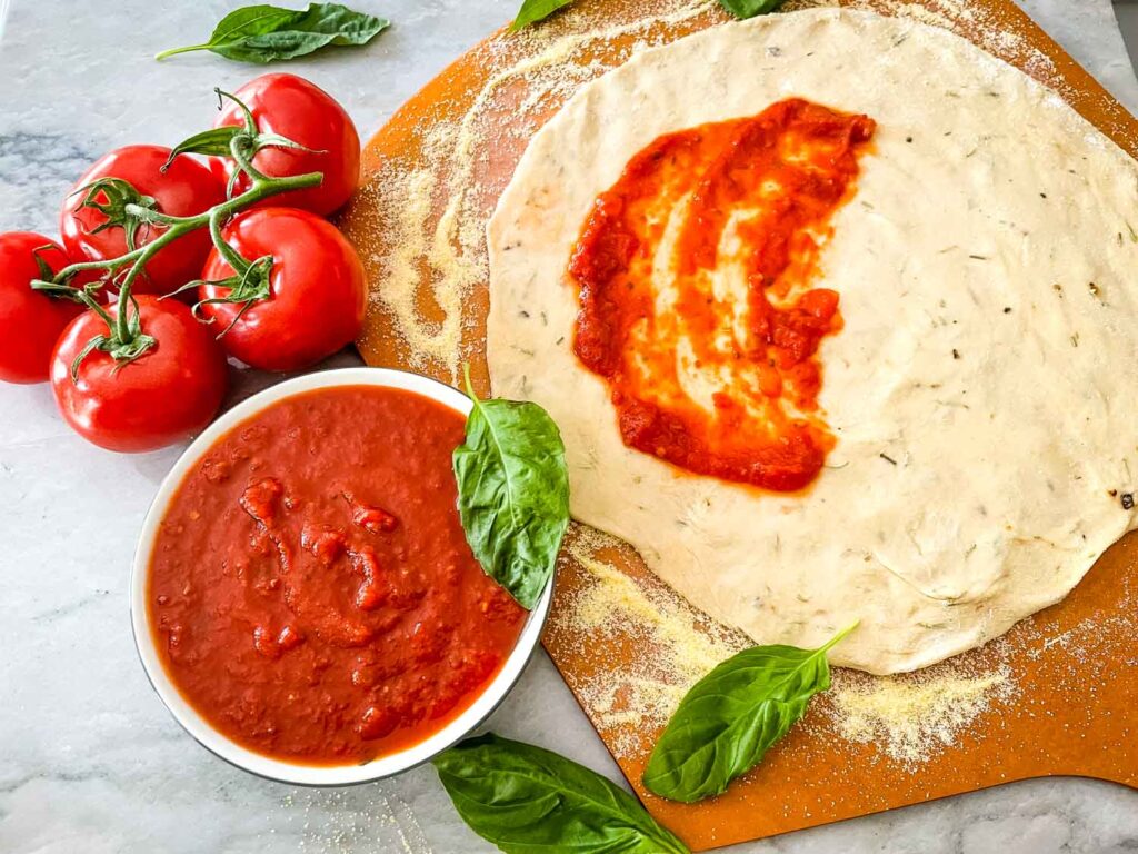 Homemade Pizza Sauce in a bowl and being spread onto pizza dough