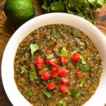 Roasted Tomatillo Salsa Verde in a white bowl with tomatoes and cilantro as a garnish. On a cutting board with cilantro and lime.