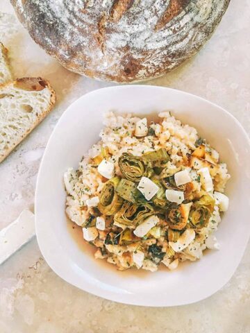 Looking down on Roasted Leek and Brie Risotto in a white bowl with bread above it on a counter