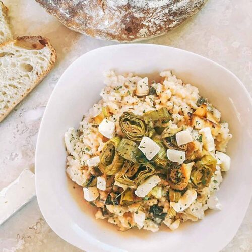 Looking down on Roasted Leek and Brie Risotto in a white bowl with bread above it on a counter