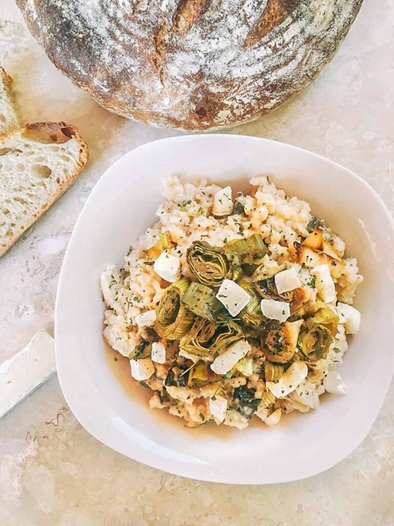 Looking down on Roasted Leek and Brie Risotto in a white bowl with bread above it on a counter