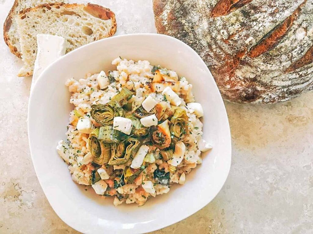 Top view of Roasted Leek and Brie Risotto in a white bowl on a counter with bread next to it