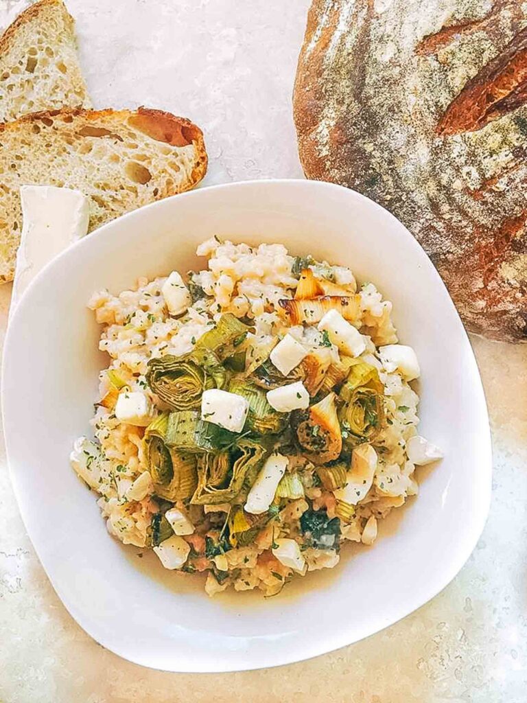 Roasted Leek and Brie Risotto in a white bowl on a counter with bread