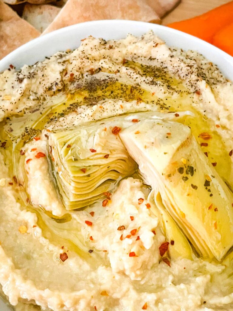 Close view of artichoke hearts sitting on a bowl of Artichoke Lemon Hummus