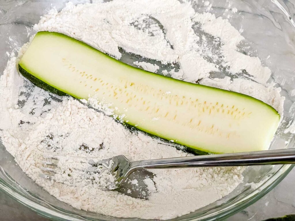 A slice of zucchini being coated in flour