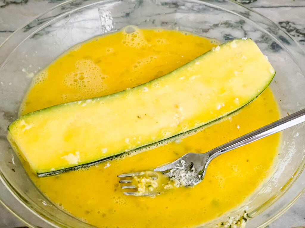 A zucchini piece being coated in the egg wash