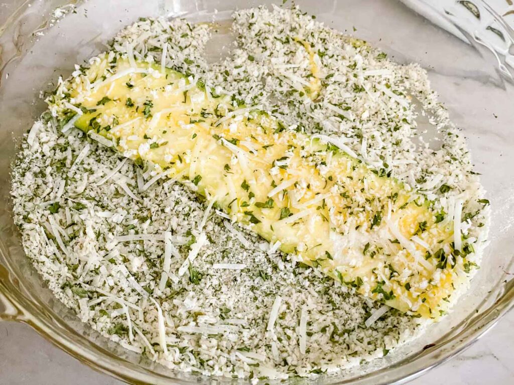 A raw zucchini piece being coated in the breadcrumb mixture