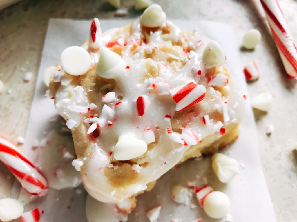 A single Peppermint White Chocolate Sweet Roll on parchment with candy canes and white chocolate chips