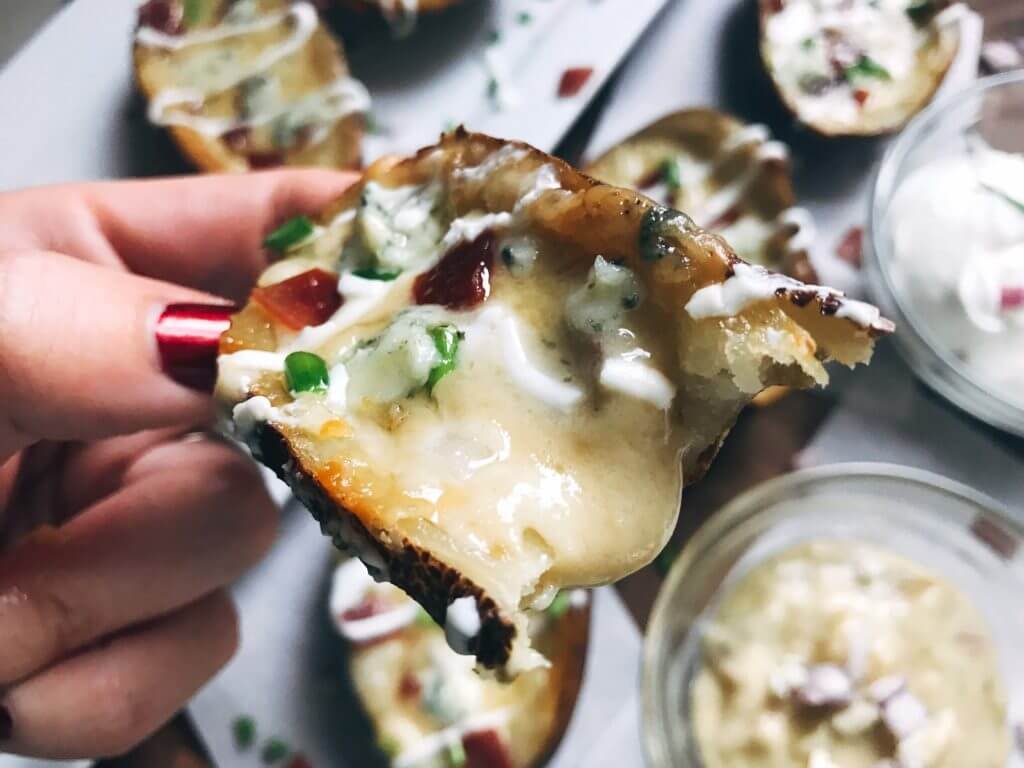 A hand holding a potato skin with the sauce coming out