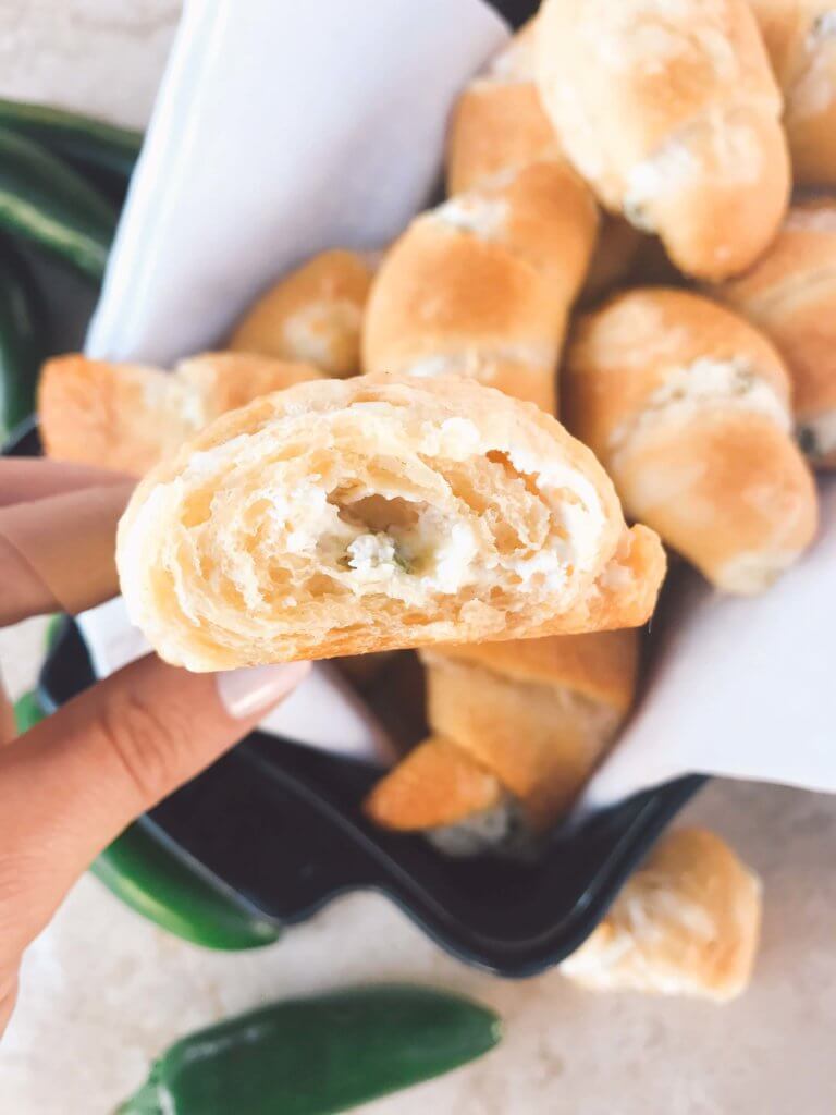 A hand holding half of a crescent roll showing cheese and peppers