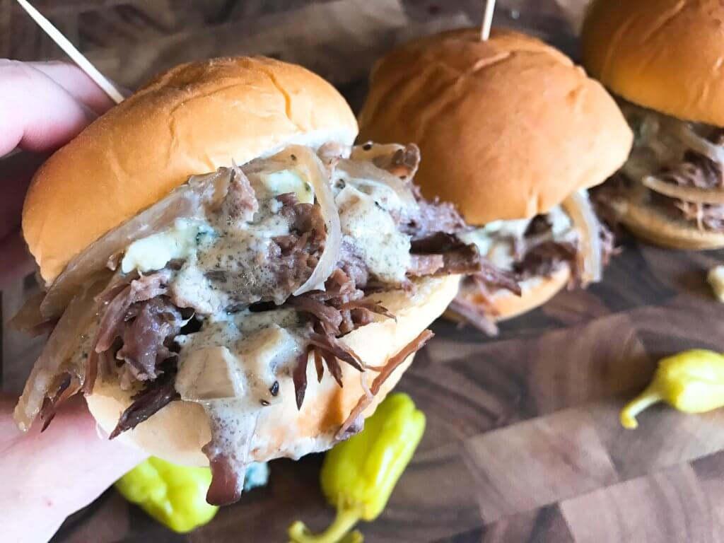 Use a slow cooker for simple and easy shredded steak sliders! Make the blue cheese sauce in advance for quick assembly. Perfect for your party, homegating, football or sport event like Super Bowl Sunday! Make them into a slider bar for customization. Kind friendly and lots of topping options like bacon, pickles, pepperoncini, and more! Bourbon Blue Cheese Steak Sliders | Three Olives Branch | www.threeolivesbranch.com