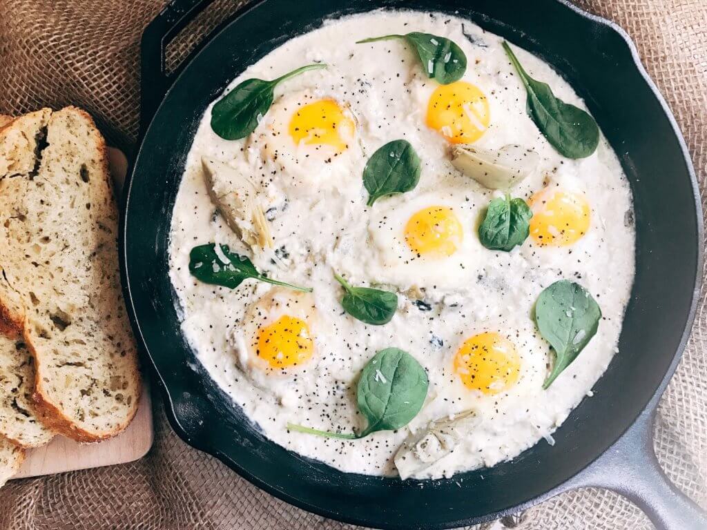 Less than 30 minutes for a simple, filling vegetarian dish that is perfect for breakfast, brunch, lunch or dinner. Also called Eggs in Purgatory, this twist on a classic dish is fast and easy and based on spinach artichoke dip. A creamy Parmesan cheese sauce is the base for the eggs, spinach, artichoke, and cheeses. Serve on top of bread for a filling meal! Spinach Artichoke Shakshuka | Three Olives Branch | www.threeolivesbranch.com