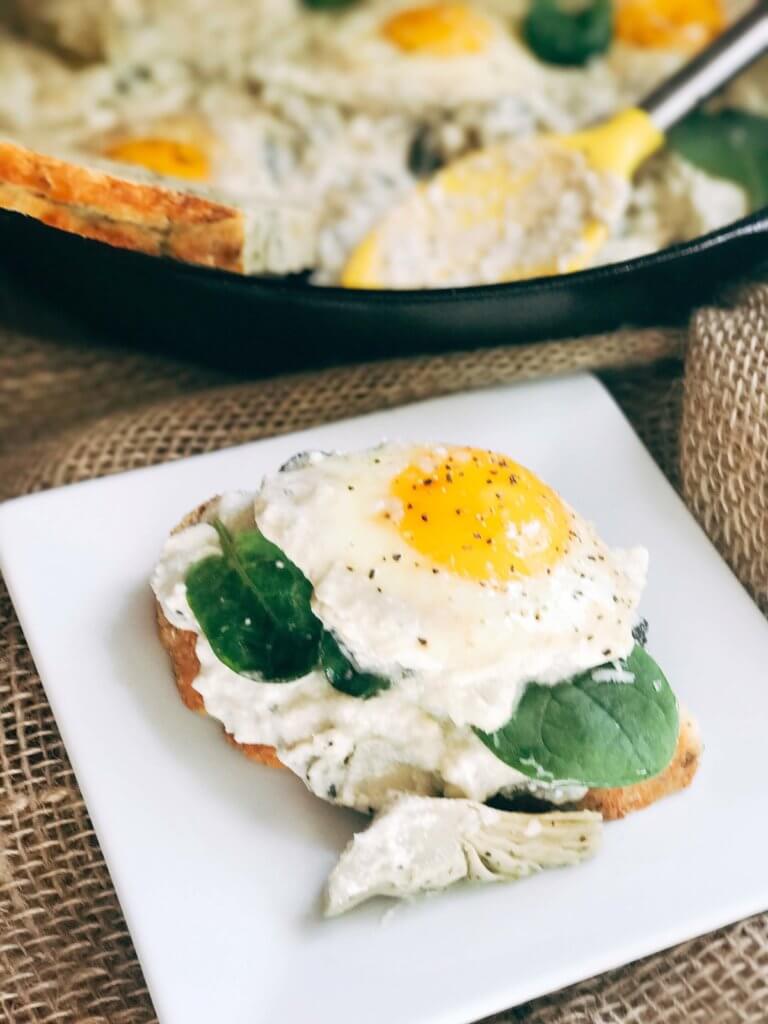 Less than 30 minutes for a simple, filling vegetarian dish that is perfect for breakfast, brunch, lunch or dinner. Also called Eggs in Purgatory, this twist on a classic dish is fast and easy and based on spinach artichoke dip. A creamy Parmesan cheese sauce is the base for the eggs, spinach, artichoke, and cheeses. Serve on top of bread for a filling meal! Spinach Artichoke Shakshuka | Three Olives Branch | www.threeolivesbranch.com