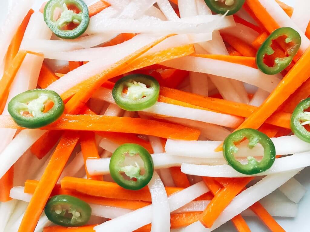 Simple and easy Spicy Vietnamese Pickled Vegetables perfect for your banh mi! Use as a quick condiment on your favorite foods. Quick refrigerator pickle of daikon radish and carrots are made spicy with serrano. A rice vinegar base is ready in just minutes for this classic Vietnamese slaw. Use cucumber or your favorite vegetables. Vegan, gluten free, and vegetarian. #pickled #banhmi #vietnamese