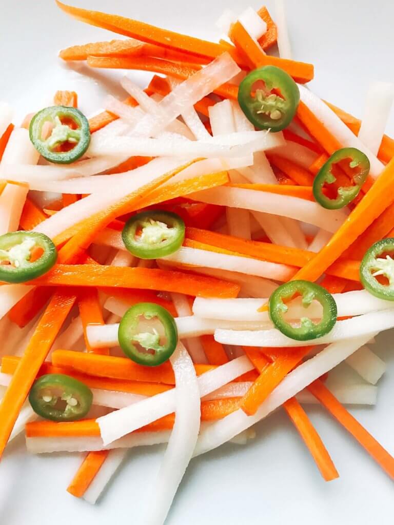 Simple and easy Spicy Vietnamese Pickled Vegetables perfect for your banh mi! Use as a quick condiment on your favorite foods. Quick refrigerator pickle of daikon radish and carrots are made spicy with serrano. A rice vinegar base is ready in just minutes for this classic Vietnamese slaw. Use cucumber or your favorite vegetables. Vegan, gluten free, and vegetarian. #pickled #banhmi #vietnamese