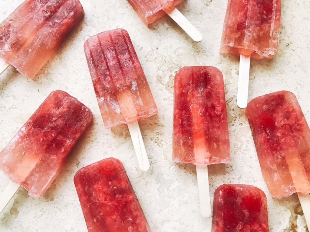 Popsicles made of rosé wine and raspberries! Simple to make and a great alcoholic adult treat for the warm and hot summer days. A twist on the frosé (frozé) trend, putting your favorite pink rose wine in popsicle form. A perfect treat or poptail for a cookout, barbecue, or grilling day. BBQ parties never tasted so good! Cocktail on a stick. Raspberry Rosé (Frosé) Popsicles | Three Olives Branch | www.threeolivesbranch.com