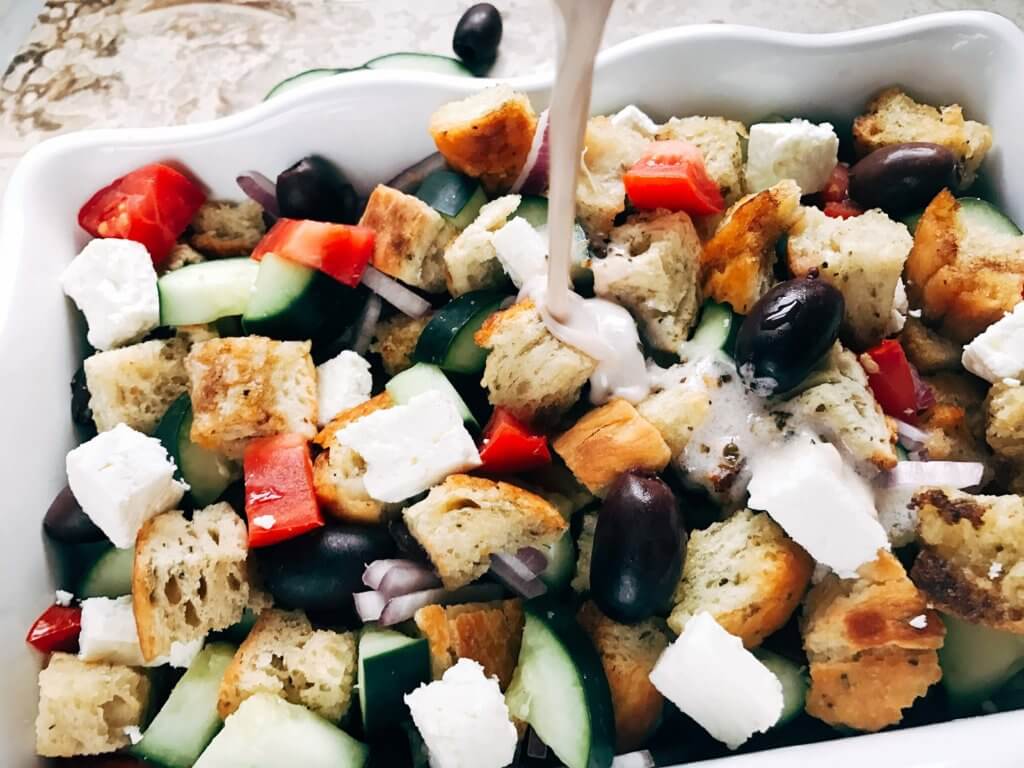 Traditional Italian salad combined with a Greek salad. Simple to make and a perfect side dish for your summer grilling party or BBQ gathering, Father's Day, 4th of July, and more. Bread chunks are tossed with Greek salad ingredients of feta cheese, kalamata olives, red onion, cucumber, and tomatoes with a creamy vinaigrette made from Greek yogurt, oregano, oil, and red wine vinegar. Simple to make and a unique side dish to show off! Creamy Greek Panzanella Salad | Three Olives Branch | www.threeolivesbranch.com