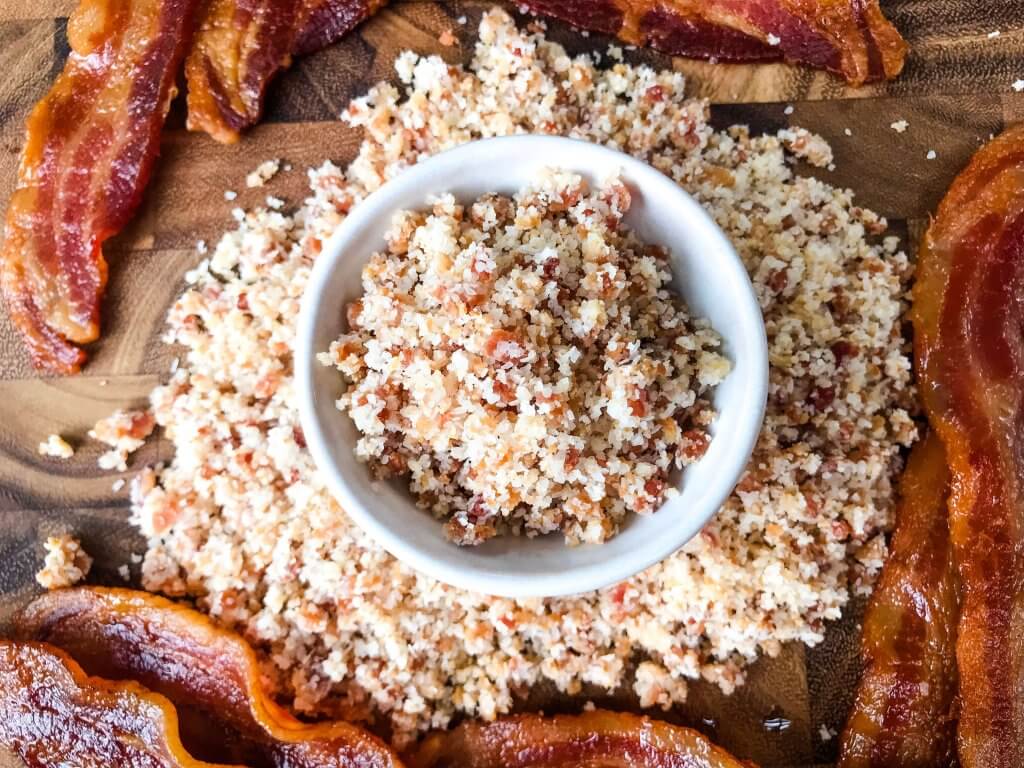 Top view of Bacon Bourbon Flavored Salt in a small bowl surrounded by more salt and bacon strips