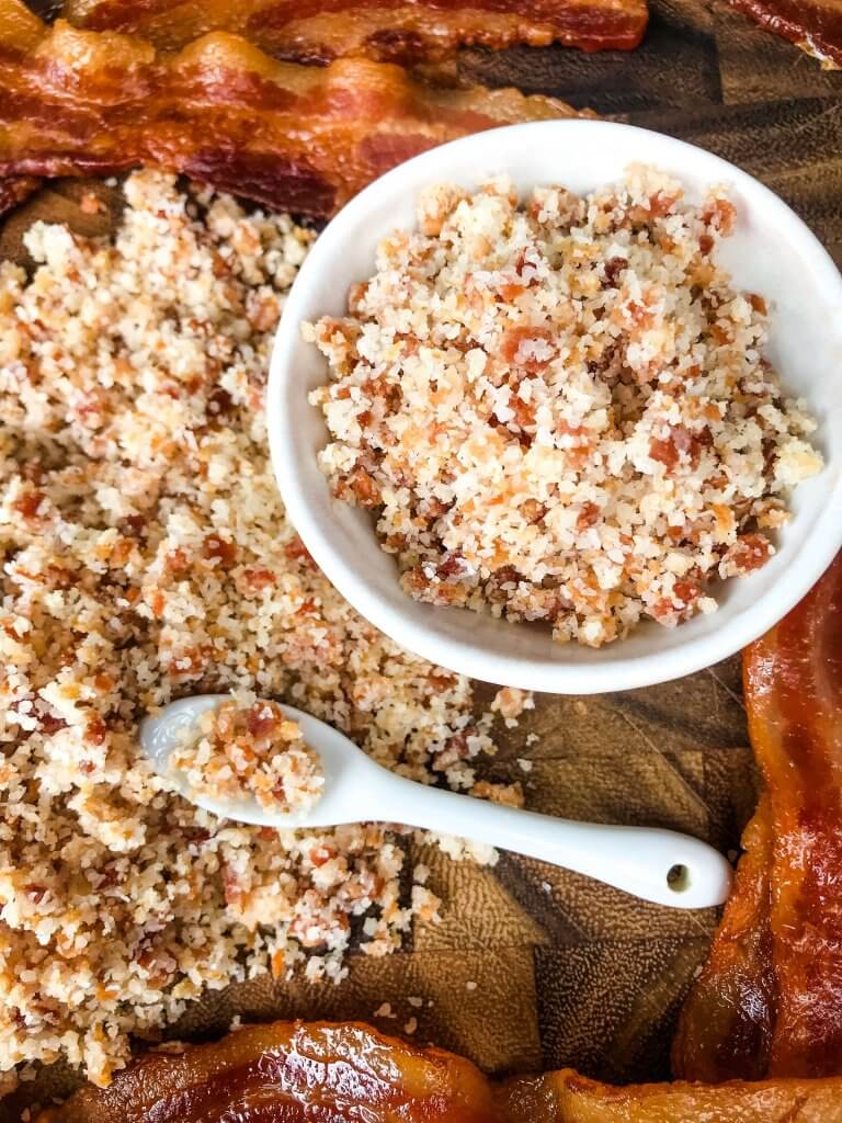 A small bowl filled with bacon salt next to a pile of the salt and bacon strips