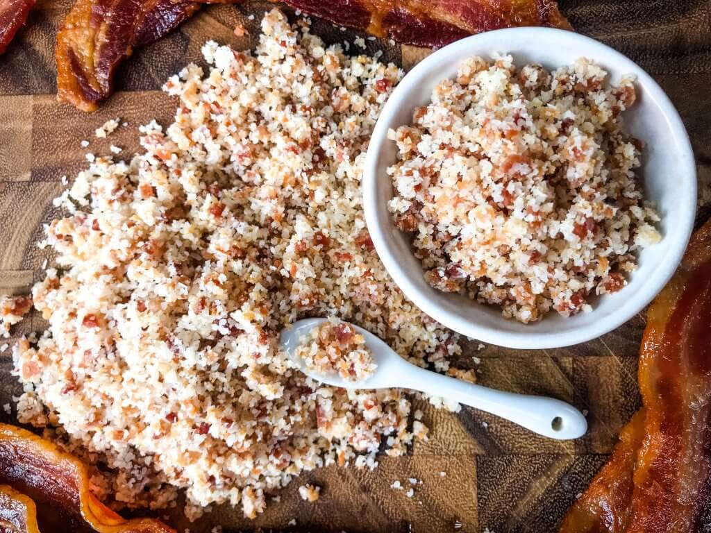 Top view of bacon salt in a bowl and a pile of it next to it with a spoon