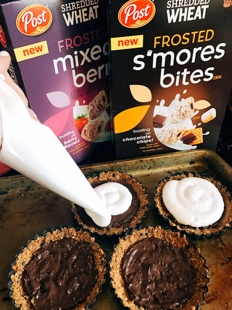 A fun dessert perfect for summer activities like 4th of July and camping. A graham cracker crust is made out of ground Post Shredded Wheat Frosted S'mores Bites Cereal, then filled with melted chocolate, marshmallow fluff, and topped off with some decorations. A fun sweet treat in an individual tart. Individual S'mores Tarts | Three Olives Branch | www.threeolivesbranch.com