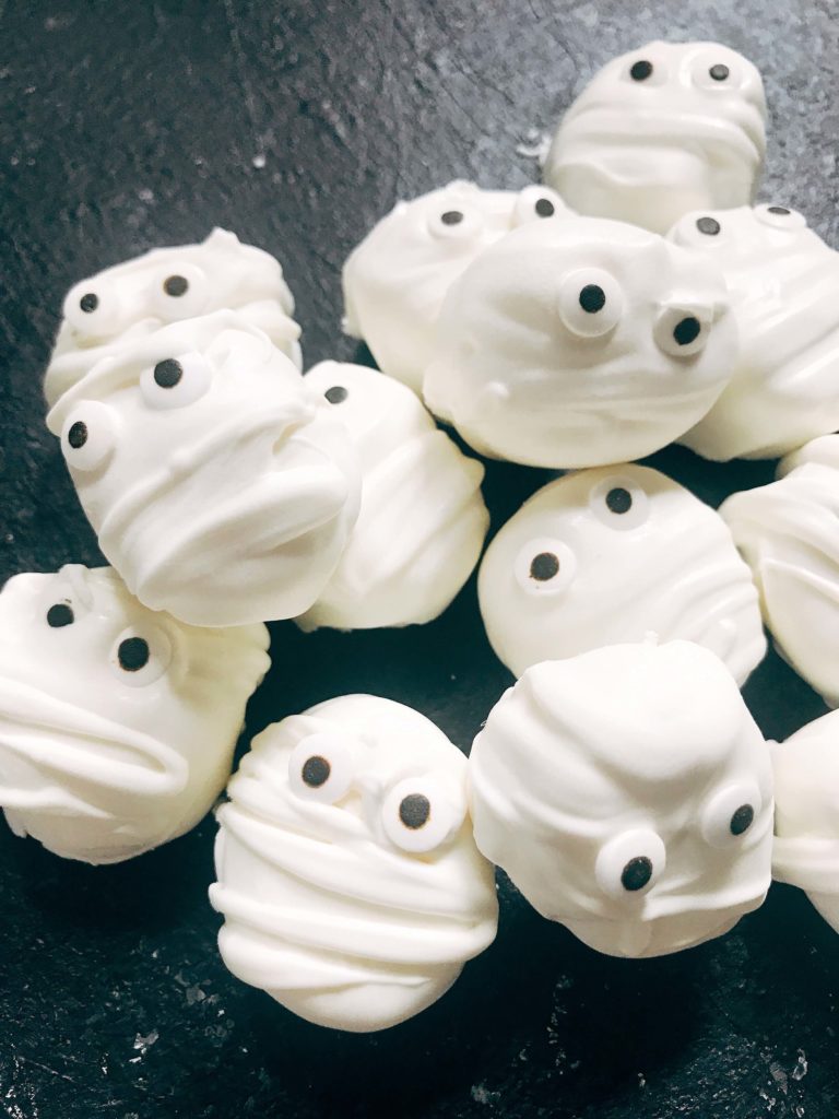 15 minutes to make these quick and simple mummy marshmallows! Large marshmallows are cut in half, covered in white candy melt with mummy wraps, and small candy eyes. Perfect for Halloween parties and a favorite among kids. Halloween Mummy Candy Dipped Marshmallows | Three Olives Branch | www.threeolivesbranch.com