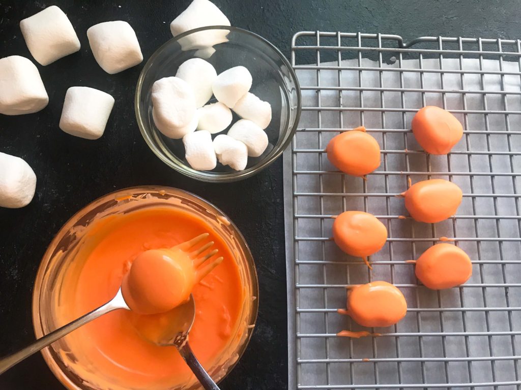 Candy pumpkin marshmallows, perfect for Halloween! Marshmallows are coated in melted orange candy with black piping gel for their jack-o-lantern faces. A fun dessert treat to make for Halloween parties. Halloween Candy Dipped Jack-O-Lantern Pumpkin Marshmallows | Three Olives Branch | www.threeolivesbranch.com #halloween #marshmallow #pumpkin #jackolantern