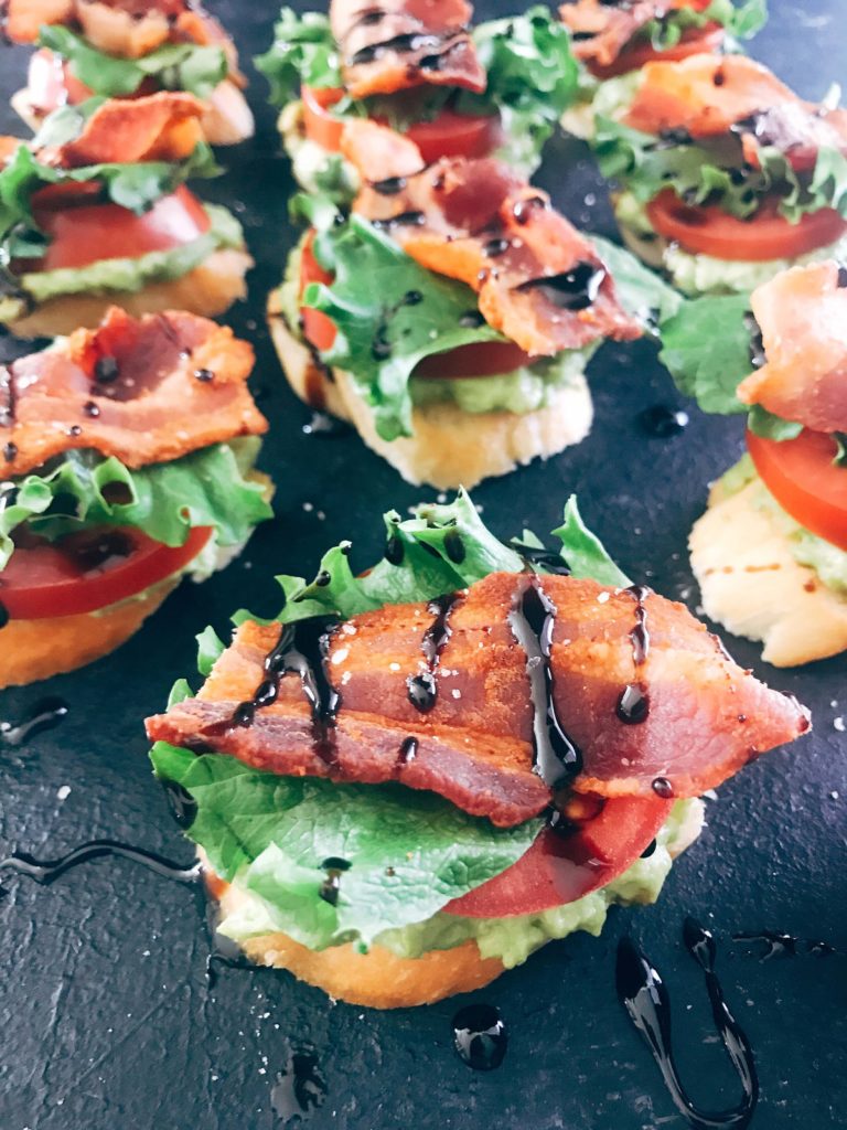 Quick and simple party appetizers. A twist on the BLT sandwich, these mini toasts are layered with avocado, tomato, lettuce, bacon, balsamic glaze, and some seasoned salt. Easy entertaining recipe. Avocado BLT Crostini | Three Olives Branch | www.threeolivesbranch.com #appetizer #blt #partyrecipe