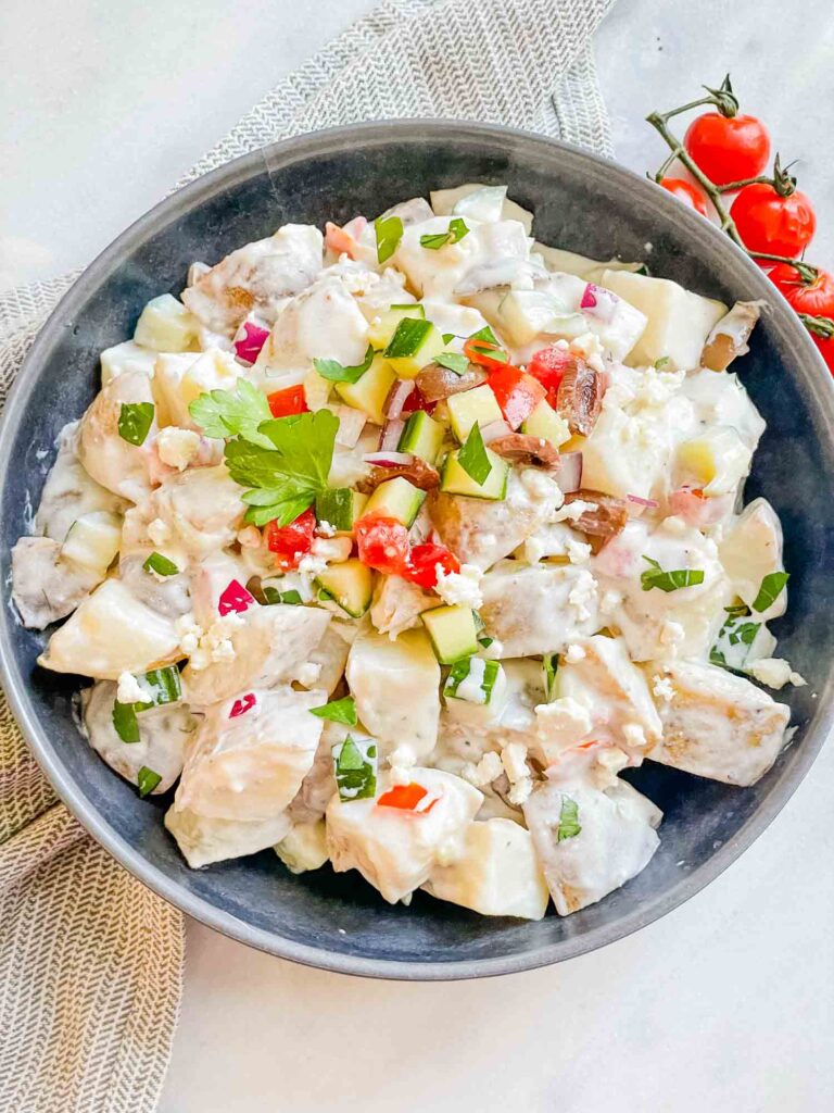 Top view of Greek Tzatziki Potato Salad in a gray bowl on a white conter with extra mix ins on top