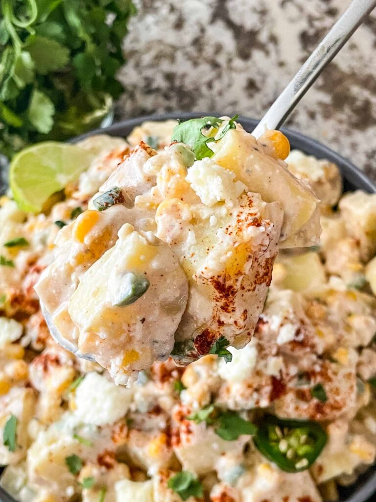 A spoon scooping some Mexican Street Corn Potato Salad out of the bowl