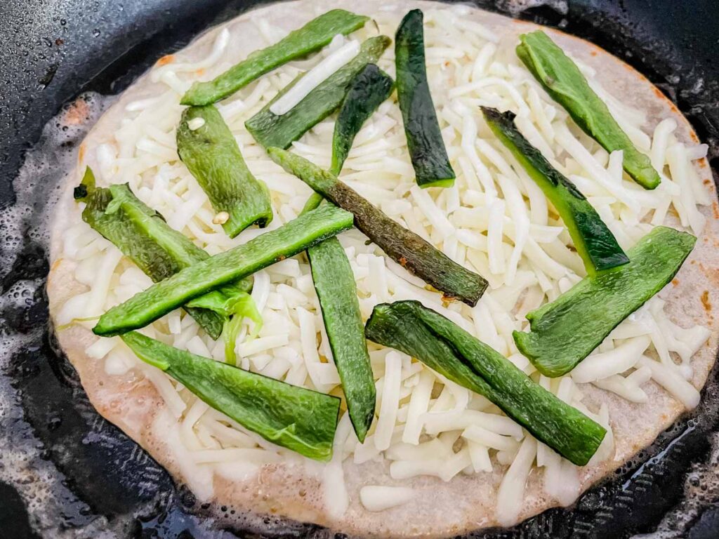 A tortilla cooking in a skillet with the peppers and cheese on it