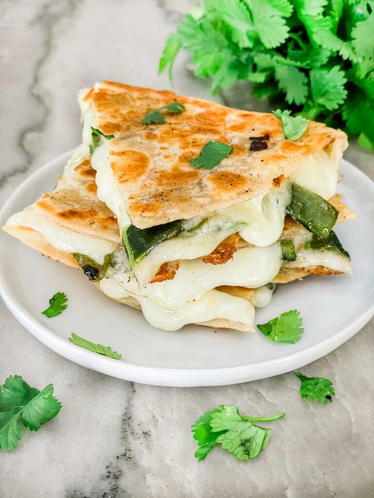 Pieces of Chile Relleno Quesadilla staked on a white plate on a counter with cilantro around it