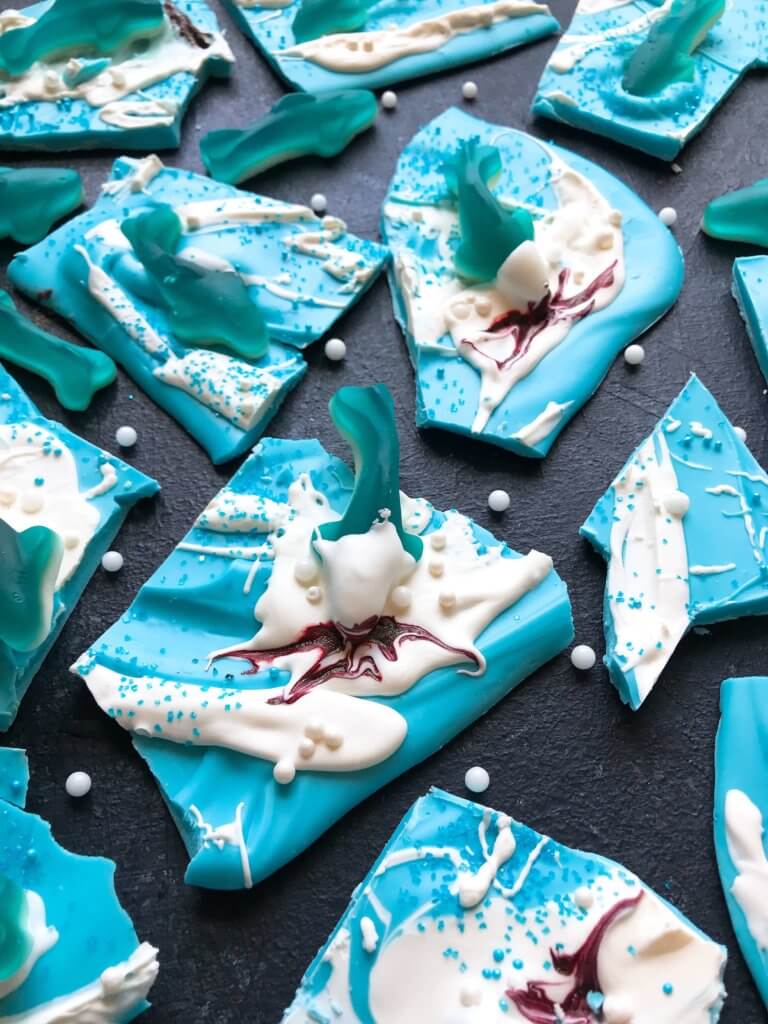 Just 10 minutes to make Shark Bark! Candy melts with sprinkles, gummy sharks, and a shark attack scene using red food gel. Gluten free (GF) quick and easy dessert recipe for shark or ocean party. Shark Week Shark Bark | Three Olives Branch | www.threeolivesbranch.com #sharkweek #ocean #sharkattack