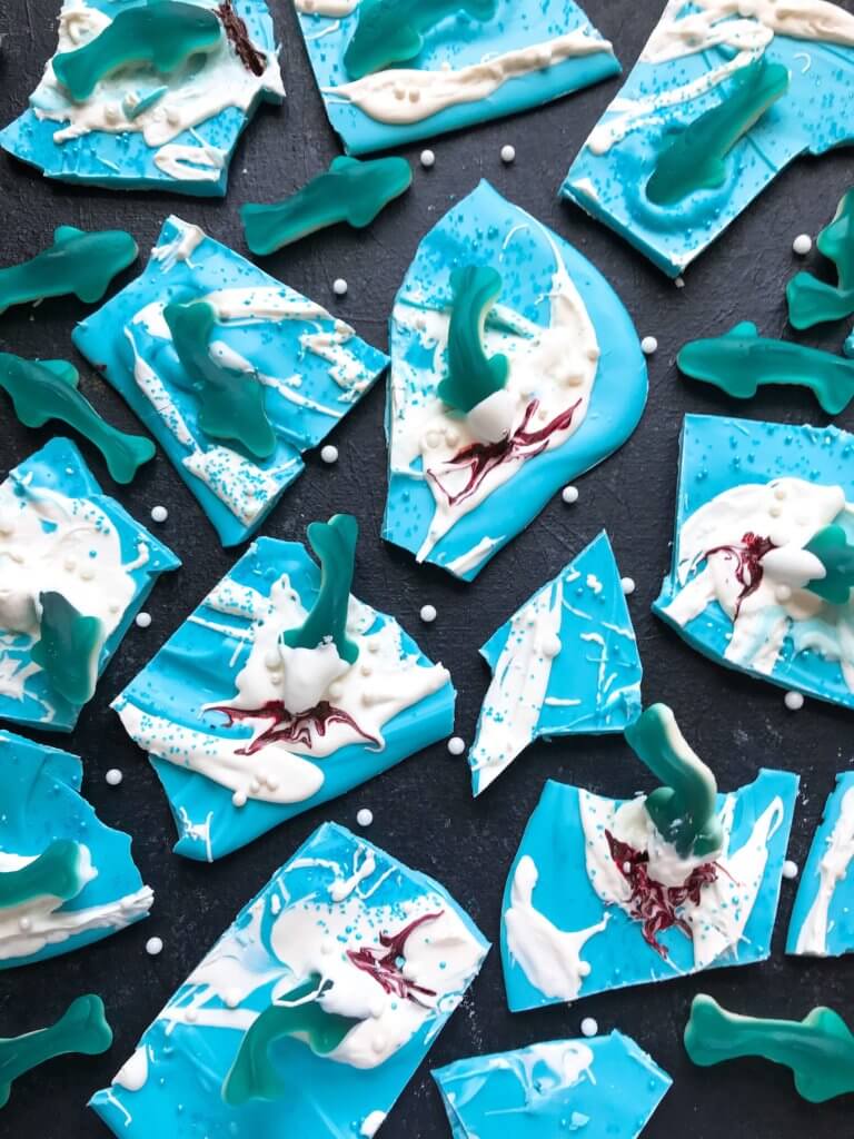 Just 10 minutes to make Shark Bark! Candy melts with sprinkles, gummy sharks, and a shark attack scene using red food gel. Gluten free (GF) quick and easy dessert recipe for shark or ocean party. Shark Week Shark Bark | Three Olives Branch | www.threeolivesbranch.com #sharkweek #ocean #sharkattack