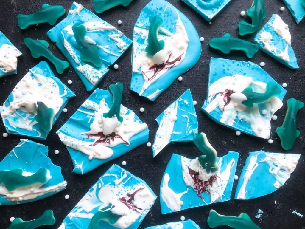 Just 10 minutes to make Shark Bark! Candy melts with sprinkles, gummy sharks, and a shark attack scene using red food gel. Gluten free (GF) quick and easy dessert recipe for shark or ocean party. Shark Week Shark Bark | Three Olives Branch | www.threeolivesbranch.com #sharkweek #ocean #sharkattack