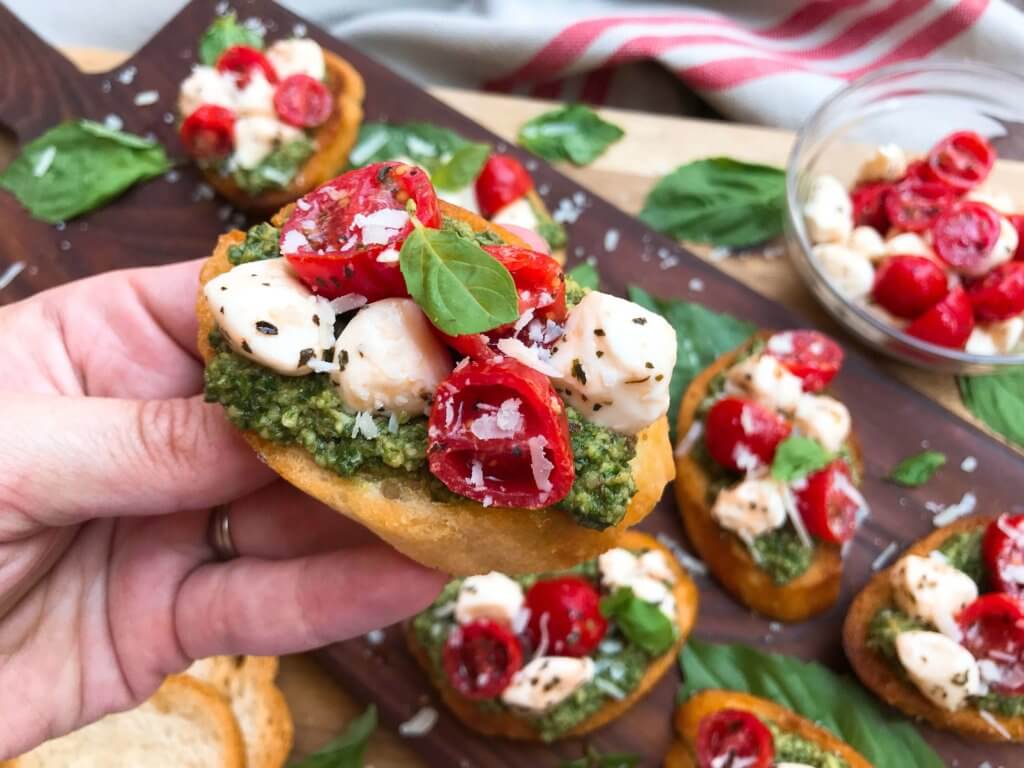 A hand holding a Caprese Pesto Crostini