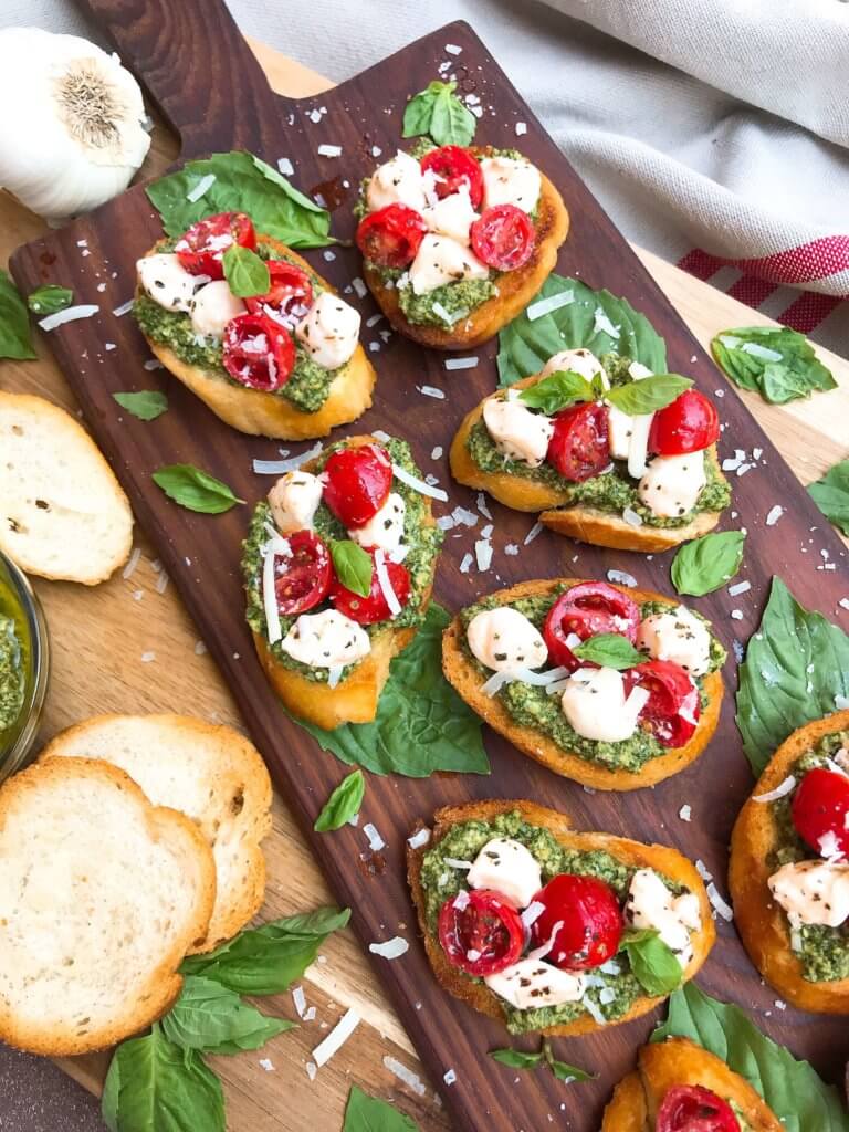 A wood board full of Caprese Pesto Crostini pieces