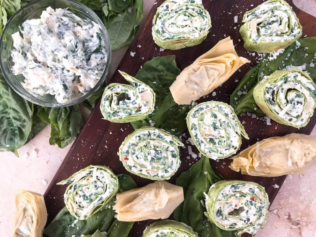 Spinach Artichoke Dip Pinwheels spread out on a wood board with artichoke hearts