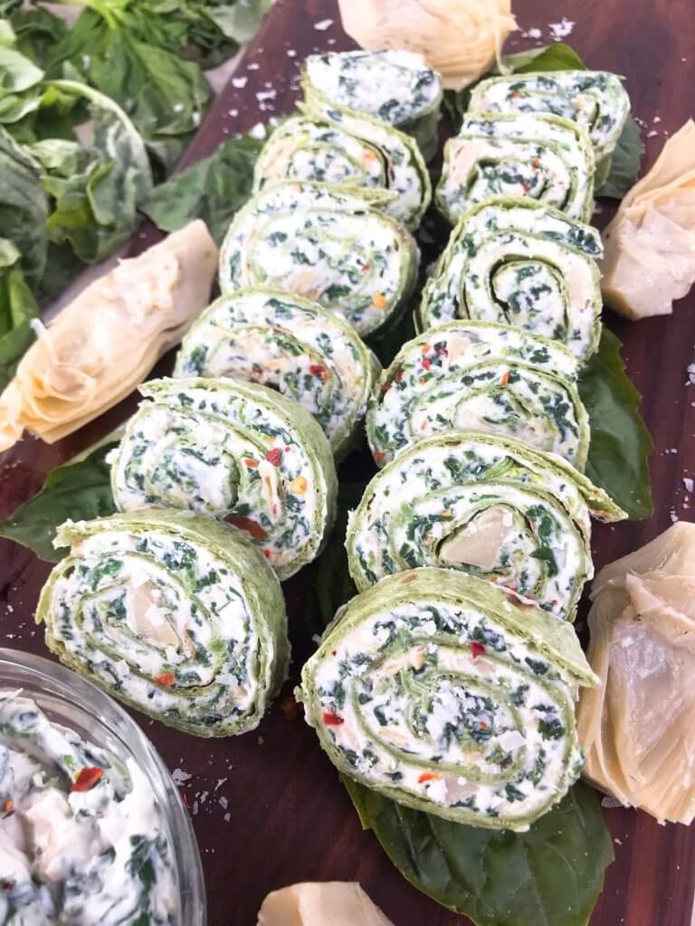 Sliced Spinach Artichoke Dip Pinwheels in two rows on a wood board